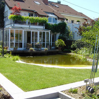 Blick vom Garten auf Wintergarten mit Terrasse über einem Teich